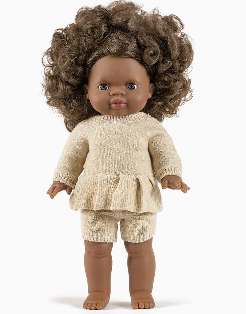 A Minikane Doll Clothing | Vito Shorts in Cream Knit with dark brown curly hair, brown skin, and brown eyes is dressed in a beige knit top with a peplum hem and matching shorts. The doll stands upright against a plain white background.