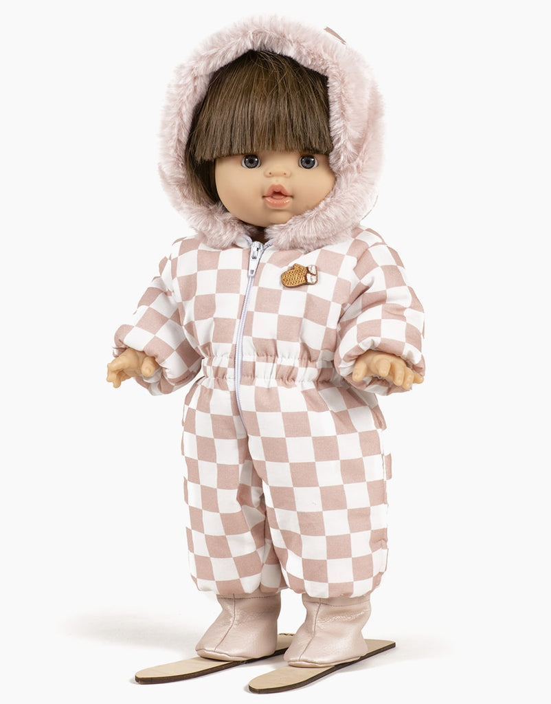 A Minikane Gordis doll with short brown hair wears the Gigi Pink and White Checkered Ski Suit, complete with a fur-lined hood, matching pants, and boots. The set fits perfectly on toddlers 34 & 37cm. The doll stands upright with arms slightly outstretched, accessorized with the charming “Mitten” Pin.