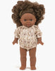 The Minikane Gordis doll, dressed in the Janelle Cotton Bertille Romper, boasts curly brown hair and a floral-patterned long-sleeved outfit. Crafted in France, this delightful doll has brown eyes and is set against a neutral backdrop. It is also hand washable for convenient maintenance.