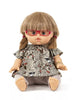 A doll with light brown hair tied in pigtails, wearing TESSA Doll Glasses by Minikane, a floral patterned dress, and light-colored leggings. The doll is seated with legs crossed and has an expressive face, perfect for imaginative play while prioritizing children's safety.