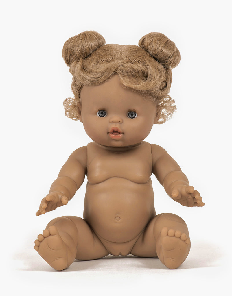 A brown-skinned Minikane Baby Doll (13") - Louise with two small buns of curly blond hair is sitting upright. The doll has blue eyes, chubby cheeks, and is unclothed, showing detailed sculpting of hands, feet, and facial features. It exudes a natural vanilla scent against the plain white background.