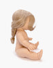 A nude Minikane Baby Doll (13") named Eleanor sits facing right, her long, light blonde hair styled in a braid. The front details of the doll and her face are hidden, while a subtle vanilla scent fills the air. She is set against a plain white background.