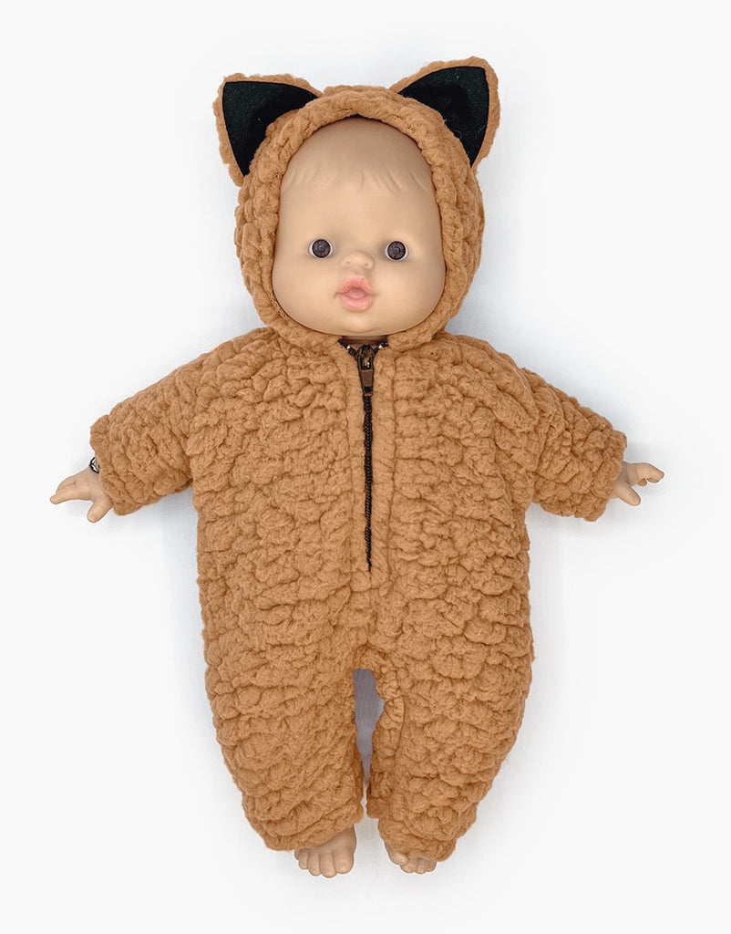 A Minikane Babies Doll cuddles up in a Brown Sugar Sherpa Costume, complete with adorable bear-like ears on the hood. The textured fabric, akin to fur, sets a cozy ambiance as the doll rests against a pristine white background.