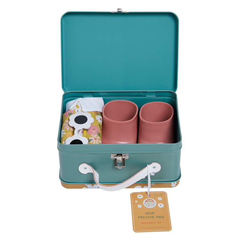 A teal and white suitcase is open, revealing two pink cups, a cloth with floral embroidered details, and a pair of novelty sunglasses. The suitcase has a latch and handle, with a tag that reads “Dinkum Doll - Sprout (Extended Pack).”