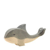 A wooden toy whale by Ostheimer Toys is depicted with a simple, handcrafted design. The whale is painted in shades of gray and natural wood, featuring minimal details like a small dot for the eye and smooth, rounded edges. This charming piece is perfect for imaginative play.