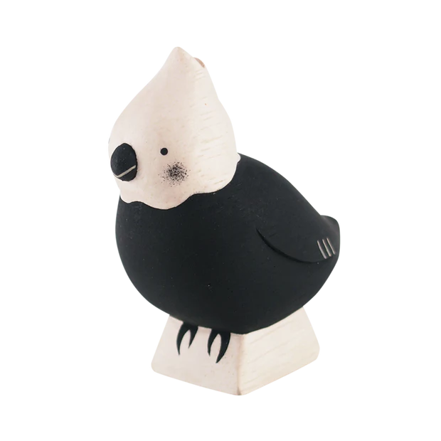 A small, handcrafted wooden parrot figurine made of Albizia wood. The parrot features a white head and black body with simple, minimalist details. It stands on a small rectangular wooden base, lending it a charming, rustic look.