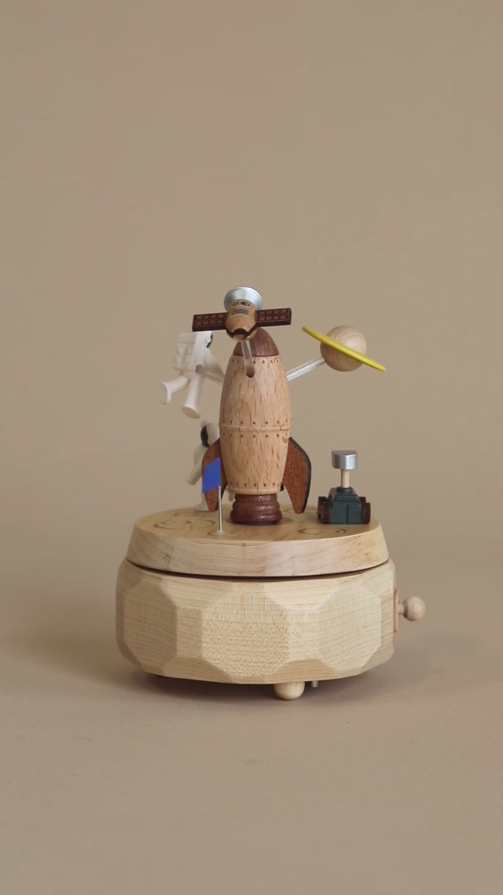 Space themed wooden music box with a rocket in the middle and astronauts and spaceships going around it. 