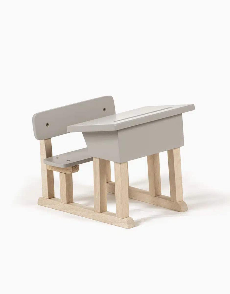 Introducing the Minikane Doll School Desk - Grey: a charming small wooden school desk with an attached bench, skillfully crafted by an artisan carpenter. The desk and bench are painted in a light grey hue, contrasting beautifully with the natural wood supporting frame. It features a slanted top and a simple backrest secured with two screws, making it ideal for Minikane Babies' playroom.