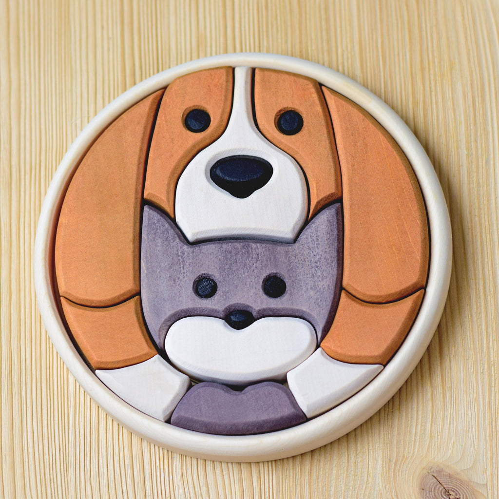 A Round Cat and Dog Puzzle set on a light wood surface, depicting an illustration of a dog with a smaller cat nestled beneath its face. The puzzle pieces, featuring natural wood markings and painted in shades of brown, white, gray, and black with non-toxic paint, fit together to form the two animals.