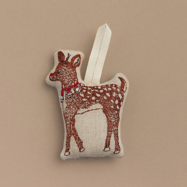 The "Rudolph Ornament" is a small, plush reindeer figure featuring embroidered details and a festive red collar, all set against a plain beige background. It includes a loop for easy hanging.