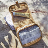 An open Olli Ella See Ya Wash Bag - Butterscotch on a sunny surface, containing sunscreen, a notepad, and other small items, displaying organized compartments.