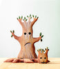 A small, handcrafted wooden sculpture from the Handmade Wooden Halloween Trees & Bat Set features two stylized trees with faces. The larger tree has a sad expression, while the smaller one in front appears content or smiling. Perfect as unique Halloween decor, they rest on a light-colored wooden surface against a plain, light background.