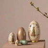 Four Maileg Easter Babushka Eggs, 5 pcs of varying sizes with intricate patterns and rabbit motifs, displayed elegantly against a neutral backdrop alongside a sprig of blooming flowers.