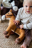 A baby sitting on a carpet with Stormy the Horse Stuffed Animal, suitable for infants.