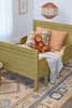 A cozy children's bedroom features a light green wooden bed adorned with plaid and peach pillows, holding two of The Orangutans Stuffed Animals. The bed is covered with a white blanket, and a decorative rug with geometric patterns lies on the floor. A wicker basket and framed art are also visible.