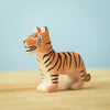 A small, handcrafted wooden tiger figurine with orange and black stripes stands on a light wooden surface against a soft blue background. The figure is meticulously carved and painted, showcasing the tiger's signature features—perfect for imaginative play or adding to your Bumbu Wooden Tiger Set.