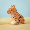 A small, hand-carved wooden tiger figurine from the Bumbu Wooden Tiger Set, adorned with orange and black stripes, sits on a wooden surface against a light blue background. The handcrafted, eco-friendly figurine features simplistic details, giving it a charming and artisanal appearance.