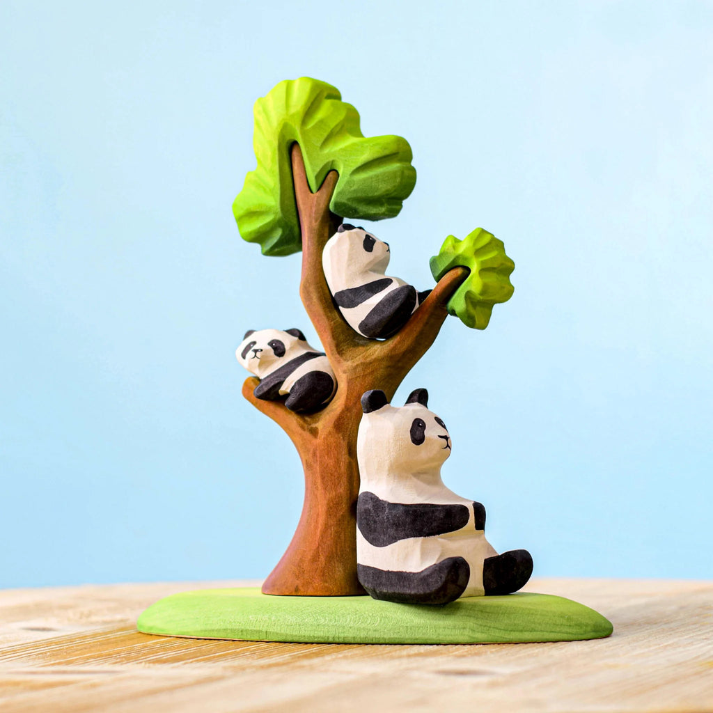 The Bumbu Panda Bears And Tree Set depicts a panda sitting at the base of a tree with two baby pandas resting on the branches. Made from eco-friendly wood and painted in simple, bright colors, it’s perfect for imaginative play scenes against a plain, light blue background.