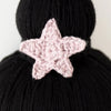 Close-up of a pink crocheted Cuddle + Kind Luna The Mermaid attached to a black hand-knit background, highlighting the detailed stitch work of the star.