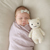 A newborn baby wrapped in a Cuddle + Kind Baby Kitten blanket, sleeping peacefully with a small, hand-knit cat toy beside her, and a cute bow on her head.