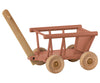 A Maileg Wagon with a simple handle, four wheels, and a slatted body, painted in light brown, isolated on a white background.