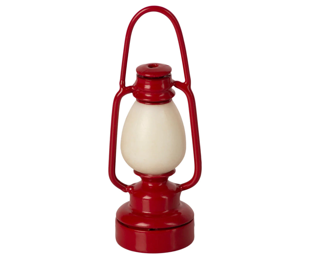 A Maileg Lantern with a white bulb in the center, designed as a miniature lantern. It has a curved handle at the top for easy carrying and a sturdy base. The design is simple and classic, reminiscent of old-fashioned oil lanterns. Note: this non-rechargeable lantern requires a battery change tool for maintenance.