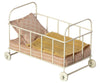 A Maileg Micro Cot with a metal frame and wheels, equipped with a pink floral mattress and a yellow knitted blanket.