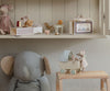 A cozy shelf displays children's toys: a large gray plush elephant, unique dolls, small wooden toys, and a Maileg Micro Pram with triplets.