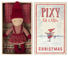 A small doll dressed in a red hat, red and white sweater, and a red skirt lies in a box with a red and white checked pillow and a striped blanket. The box reads "Maileg Pixy Elfie," complete with an image of an elf ice skating—a perfect Christmas friend for your Maileg ginger bread house.