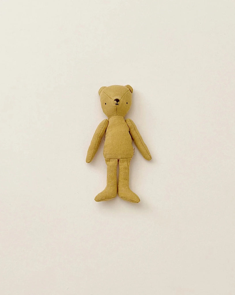 A simple Maileg Teddy Junior with a vintage look on a plain white background. The Maileg Teddy Junior has a light brown color, small black eyes, and a tiny black nose, with outstretched arms and legs. Its minimalist design captures the essence of soft linen, evoking memories of an old-time teddy bear family.