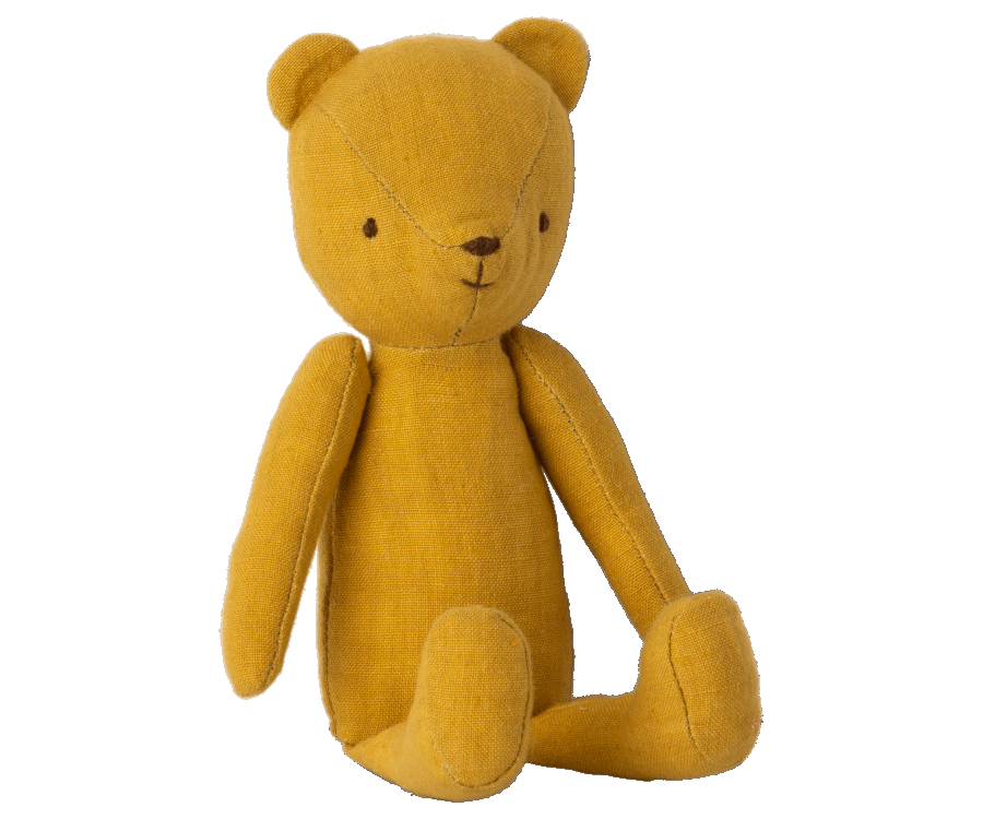 A mustard yellow stuffed Maileg Teddy Junior with simple black stitching for facial features sits upright against a plain white background. The bear, part of the Maileg Teddy Junior family, has a minimalist design with jointed arms and legs, giving it a charming vintage look.