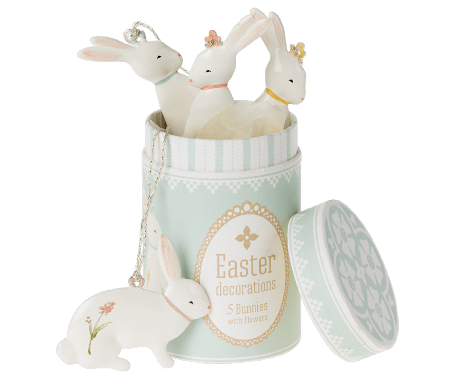 A pastel green cylindrical container labeled "Maileg Easter Bunny Ornaments, 5 pcs." has its lid off. Four sweet bunny ornaments with flower accents are inside, and one bunny ornament lies on its side beside the container.