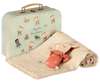 A pale green suitcase with whimsical illustrations of children playing is paired with a beige knitted blanket adorned with small pom-poms. A Bambi rattle, resembling a sleepy animal wearing an orange outfit, lies partially wrapped in the blanket. This Maileg Baby Gift Set is perfect for any little one.