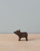 A small, dark brown wooden pig figure with simple, curved yellow lines on its side rests on a light wooden surface against a plain, light grey background. This minimalist design from Holztiger Young Boar has no visible eyes, nose, or mouth and embodies the charm of handcrafted wood toys made in Europe.