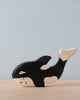 A small wooden toy shaped and painted like an orca whale, featuring black and white coloration, is placed on a light wooden surface against a plain light blue background. Handcrafted wood and part of the HOLZTIGER figures collection, this European-made toy, the Holztiger Orca Whale, boasts simplistic, minimalistic design elements.