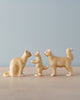 The Handmade Wooden Cat Family features three light brown cats against a light blue background: the one on the left is seated, the middle cat stands on two legs with front paws raised, and the cat on the right stands on all fours with its tail curved upward.