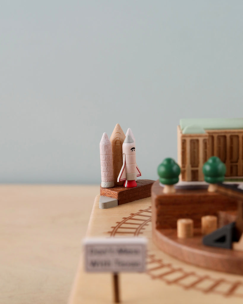 A detailed miniature model display featuring two iconic buildings, possibly historical, with a small rocket between them. In the foreground, a sign reads "space museum visit now." Soft focus background intensifies the foreground, showcasing the Texas Wooden Music Box.