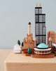 A collection of Chicago Wooden Music Box miniature models representing various unique culture landmarks displayed on a light wooden surface against a soft blue background.