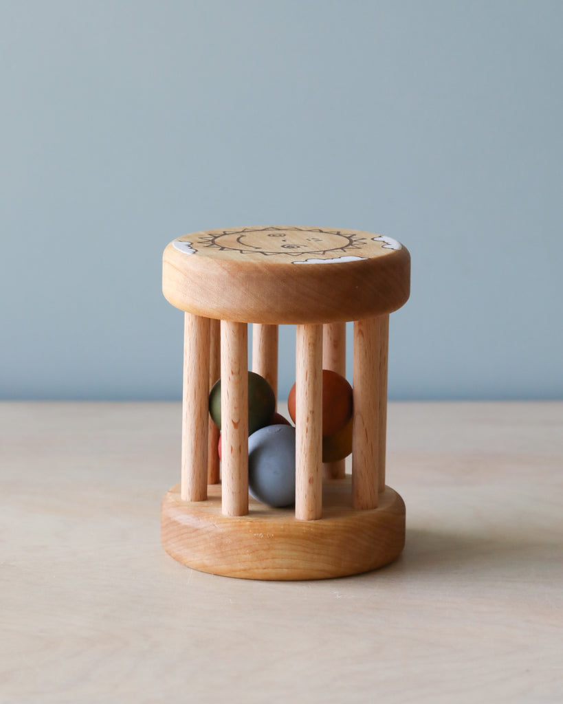 A small handmade wooden rattle crafted from sustainably harvested birch wood, with a circular seat, natural finish, and vertical dowels enclosing colorful balls, placed on a plain background.