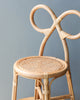 A close-up of a Toddler Rattan Bow Chair with an intricately designed backrest featuring intertwined loops, set against a soft gray background. The chair has a woven seat and light wooden frame.