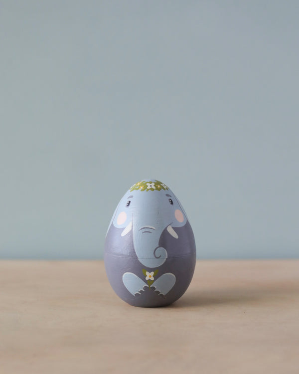 An Hand Painted Hollow Wooden Easter Egg in the shape of an elephant, with floral accents, stands against a soft blue background.