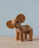 A Spring Copenhagen Ollie - Elephant toy crafted from FSC Oak with large round ears and tusks, standing against a light blue background.