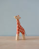 A Handmade Holzwald Giraffe - Small, crafted from high-quality materials, features a hand-painted red and white pattern and stands against a simple blue background. The giraffe appears cheerful, with a tiny tail.