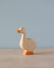 A sustainable Handmade Holzwald Goose figurine with a light body and orange beak and feet, standing against a soft blue background.