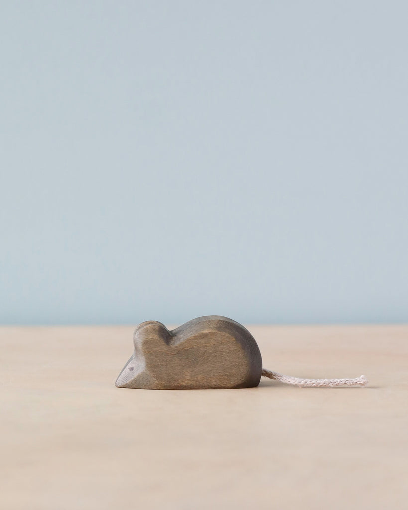 An educational Handmade Holzwald Mouse toy with a simple, streamlined design and a small white tail, set against a plain blue background on a light surface.