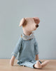 Maileg Maxi Mouse in Pyjamas, wearing light blue and white striped pajamas and a matching scarf adorned with tiny stars, sits on a light brown surface against a plain light gray background. This charming rest-time companion has its head turned slightly to the side, inviting you into its cozy world.