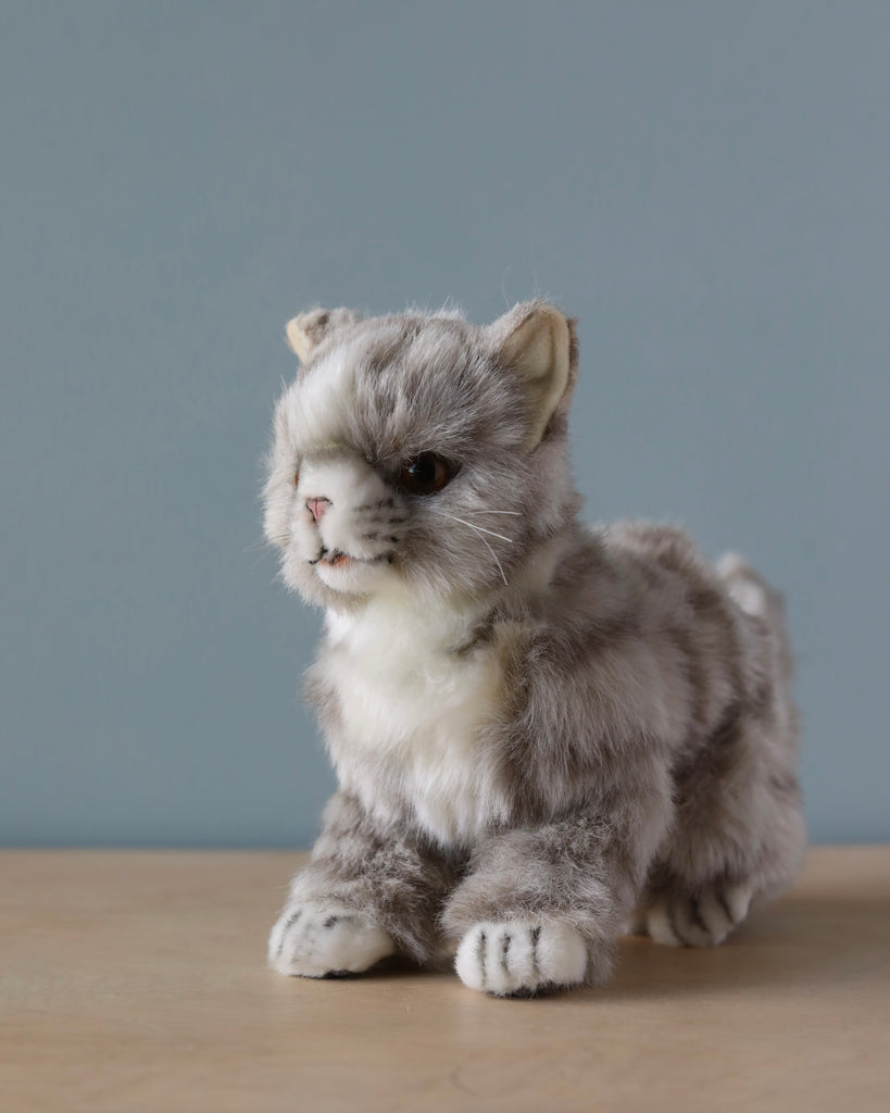 A lifelike Grey Cat Stuffed Animal sitting on a wooden surface against a plain grey background, showcasing realistic fur and sharp eyes from our collection of hand-sewn toys.