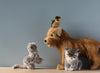 Three artisan plush animals—a koala, a dog with a bird on its head, and a Grey Cat Stuffed Animal—sit on a wooden surface against a plain gray background.