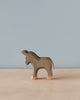 A Handmade Holzwald Small Donkey stands on a plain surface against a light blue backdrop, featuring textured wood and visible grain, with a contrasting smooth, white tail.