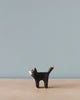 Sentence with product name: A minimalist photo featuring a small, Handmade Holzwald Black Cat against a light blue background. The cat has simplified, geometrical shapes and a visible wood grain pattern.